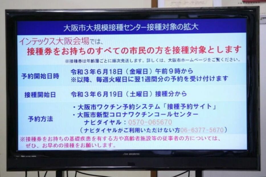 [写真]会見場に掲示された大阪市のインテックス大阪会場での接種対象を拡大についての説明