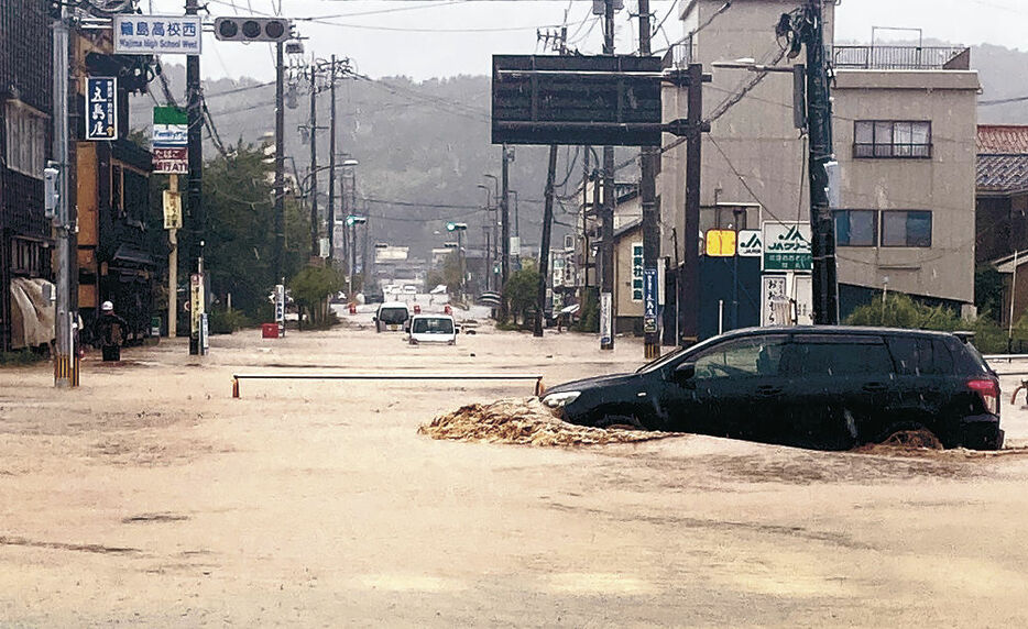 輪島市中心部の冠水した道路を走る車＝２１日午前１１時半、同市河井町