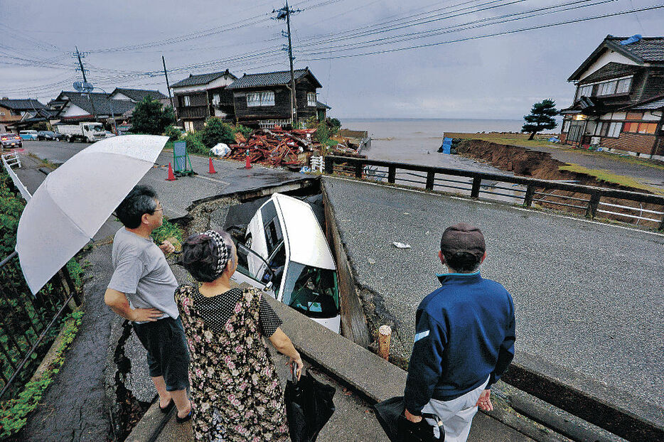 陥没した道路を見る住民＝２１日午後、珠洲市上戸町寺社