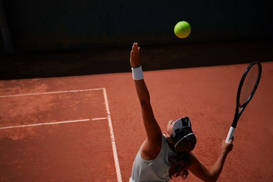 クレーコートでの試合中、サーブするテニス選手。（PHOTOGRAPH BY WUNDERVISUALS, GETTY IMAGES）