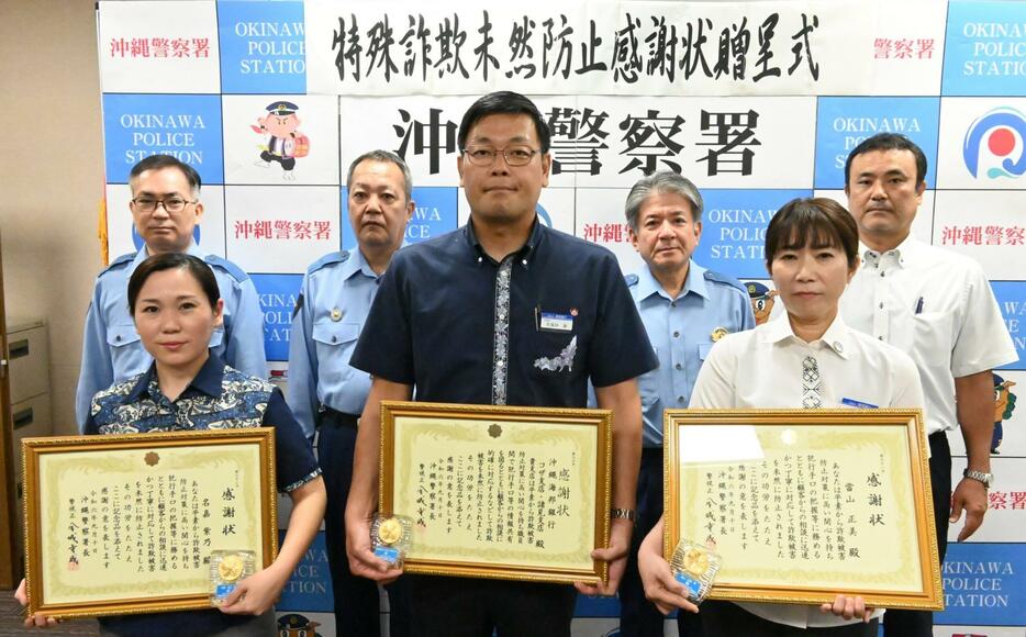 沖縄署の金城重成署長（後列右から２人目）から感謝状を受け取った沖縄海邦銀行コザ支店の久保田康支店長（前列中央）と同店行員の當山正美さん（同右）、名嘉紫乃さん（同左）ら＝10日、沖縄市