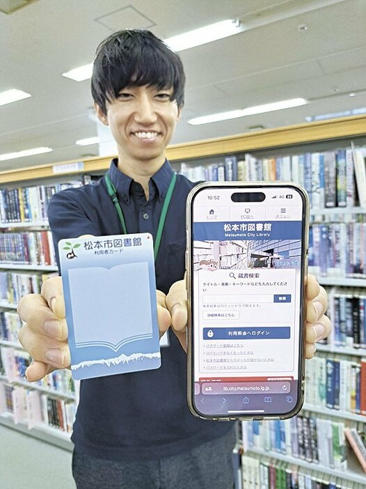 利用者カード（左）と市図書館のホームページを表示したスマホを持つ図書館職員