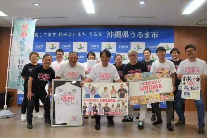 Tシャツをアピールするうるま市観光物産協会副理事長の仲西洋陽さん（左から2人目）と青柳武治さん（同4人目）、中村正人うるま市長（同3人目）ら＝8月26日、うるま市役所