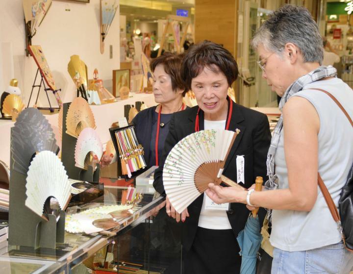 扇子を広げ、あおぎ心地を確かめる買い物客（右）＝18日午前、松山市湊町5丁目