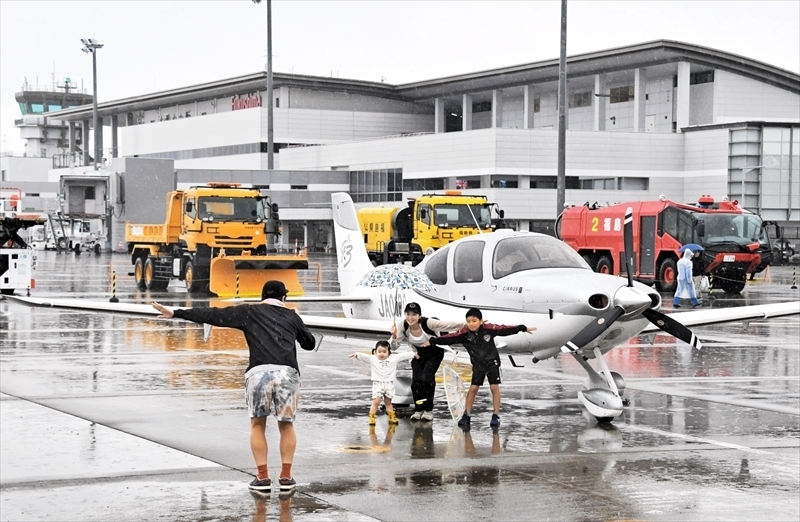 エプロンに展示された小型飛行機の前で記念撮影する家族連れ