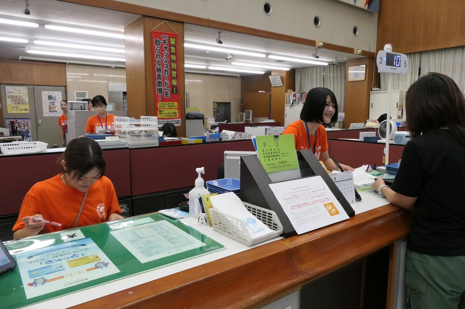 オレンジ色のTシャツを着て啓発する職員＝岡山県津山市、津山信用金庫本店で