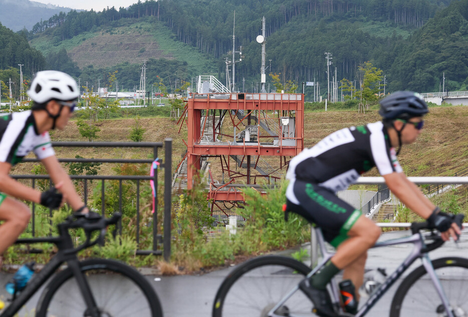 東日本大震災からの復興などを支援する自転車イベント「ツール・ド・東北２０２４」で、震災遺構「旧防災対策庁舎」近くを駆け抜ける参加者＝１５日午前、宮城県南三陸町