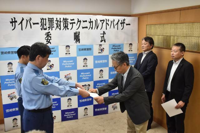 県警の平居秀一本部長（左）からサイバー犯罪対策テクニカルアドバイザーの委嘱状を受け取った３人