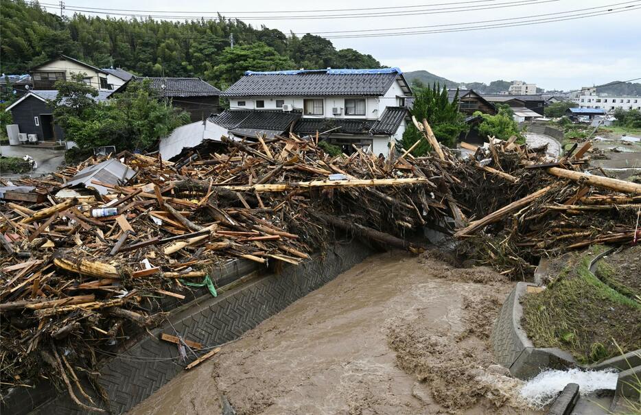 豪雨で増水した石川県輪島市の塚田川沿いで、家屋の前に積み重なった無数の流木＝22日午前11時19分