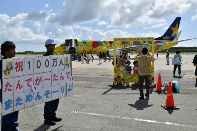 関係者らが累計搭乗者100万人達成を祝うメッセージボードを手に搭乗客を見送った＝12日、下地島空港