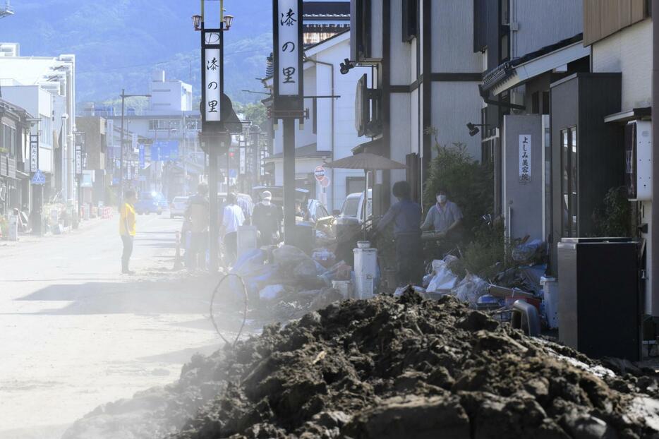 泥が乾燥し砂ぼこりが舞う中、片付けに追われる人たち＝25日午前、石川県輪島市