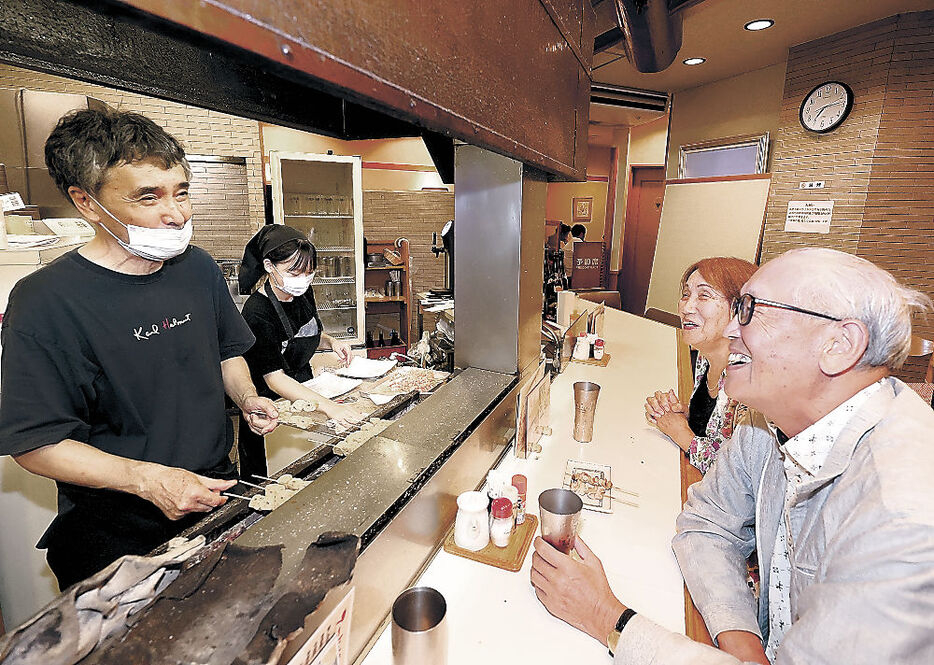 閉店を知って訪れた人と会話しながら焼き鳥を用意する田幡さん（左）