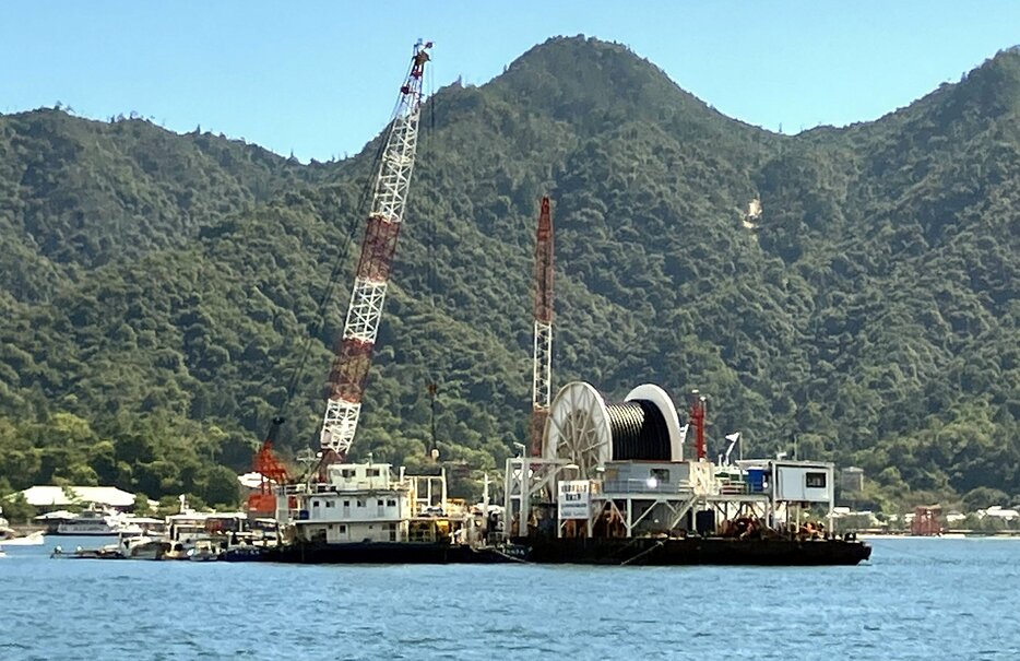 海底送水管が巻かれたドラムを載せた台船。奥は宮島