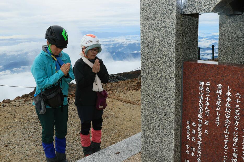 剣ケ峰の慰霊碑に手を合わせる登山者＝27日午前8時17分