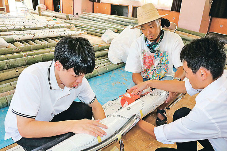 竹筒に設計図を巻き、穴を開ける箇所を確かめる池田さん（中央）ら=旧八幡保育園