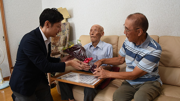 草地市長（左）から祝い状と花束を受け取る水野さん（中央）＝磐田市提供