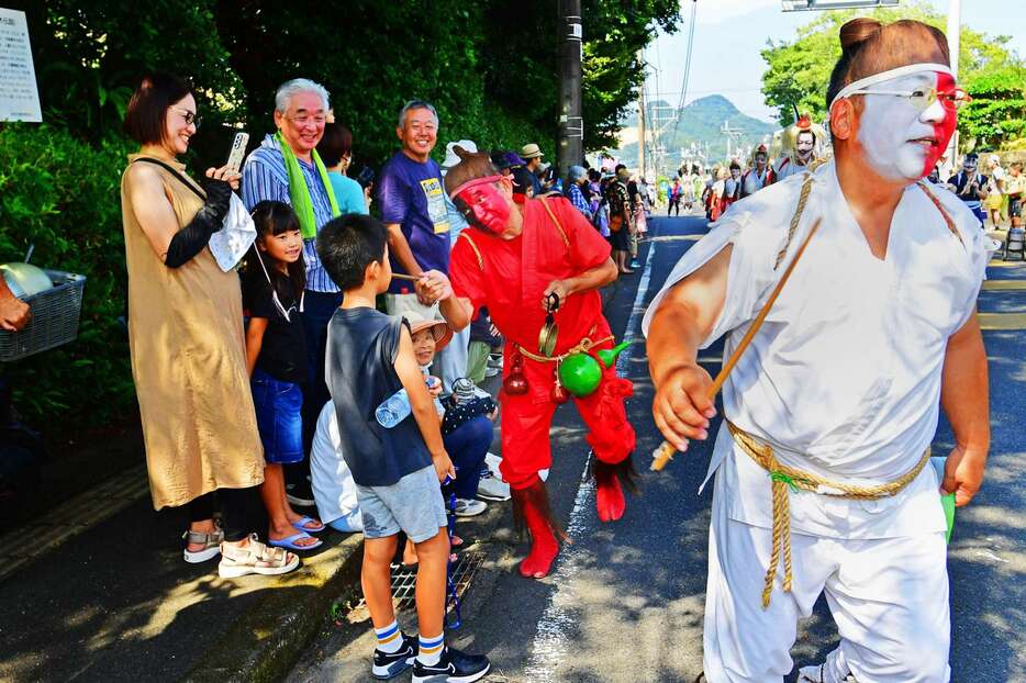 顔を半面ずつ色分けしたキツネ役が、滑稽なしぐさで観客と掛け合いながら練り歩く＝８月１６日、姶良市加治木の仮屋馬場通り