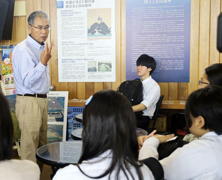 ゆりあげ港朝市協同組合の桜井広行代表理事（左）の講話を聞く石川県立輪島高の生徒たち＝28日午前、宮城県名取市