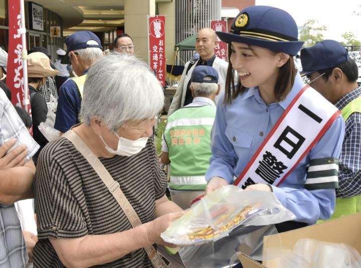 買い物客らに交通安全啓発グッズを手渡す一日署長の間瀬さん（右）