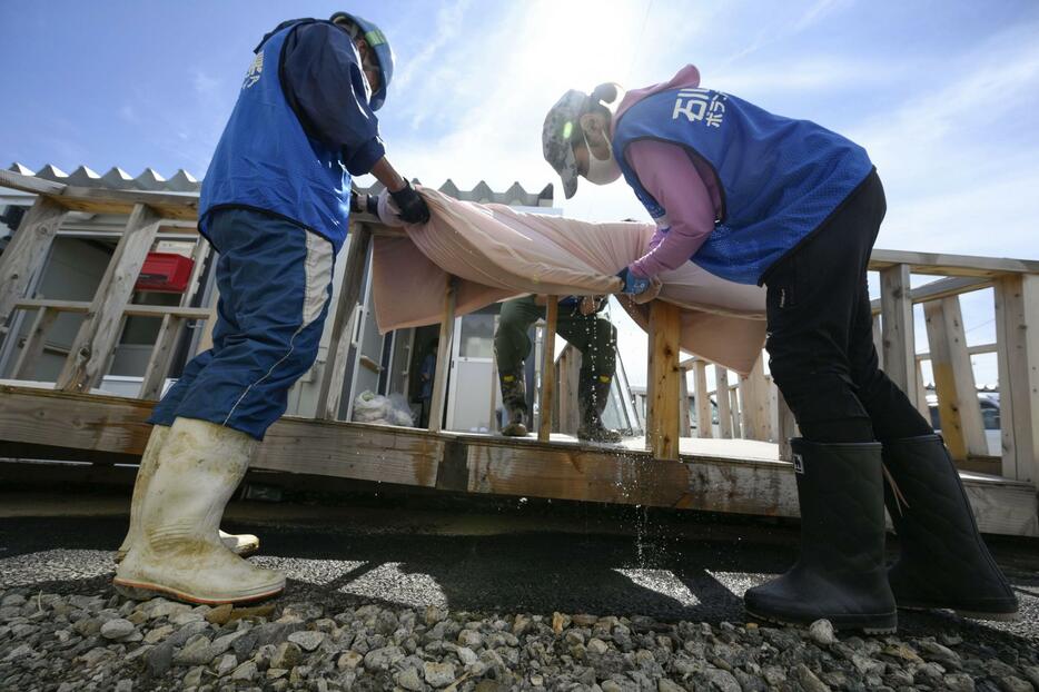 豪雨で浸水被害を受けた石川県輪島市の仮設住宅で、濡れた布団を絞る災害ボランティア＝24日午後