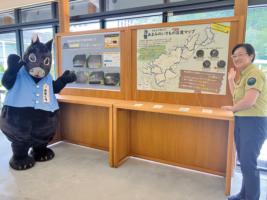 運転中の野生生物への注意を呼び掛ける環境省希少種保護増殖等専門員の鈴木真理子さん（右）と奄美野生生物保護センターのマスコットキャラクター「あまくろ」君＝20日、鹿児島県奄美市住用町