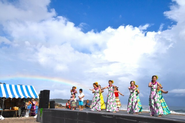 雨上がりで虹がかかる中ダンスを踊るフラガール＝下田市の吉佐美大浜海岸