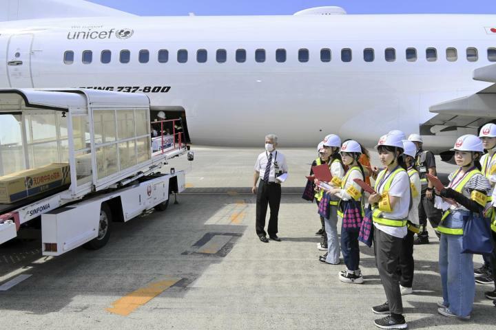 荷物の積み降ろしなどのグラハン業務を飛行機の間近で見学する学生ら＝11日午後、松山市南吉田町