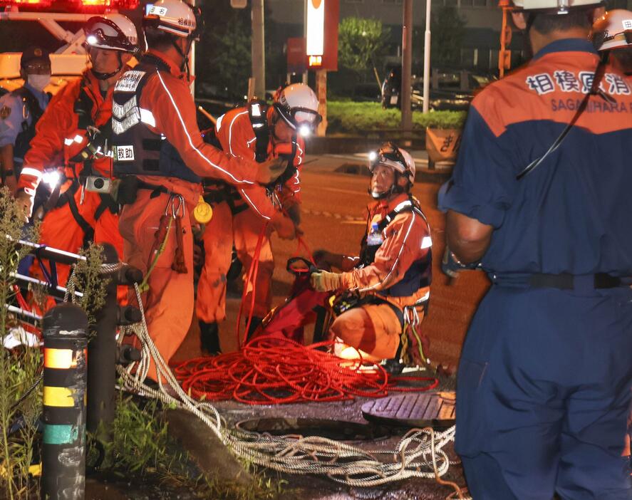 作業員2人が流された現場周辺で、下水道管を調べる消防隊員＝19日夜、相模原市