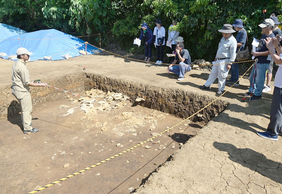 発掘現場について説明する熊本大考古学研究室の学生（左）＝3日、鹿児島県伊仙町伊仙