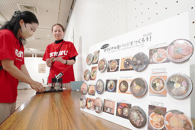 そばやラーメンに関する〝記憶〟を紹介し、缶バッジ作りもできる「ななはく！」＝山形市中央公民館