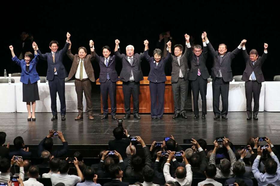 自民党総裁選の演説会で手を取り合う候補者ら。左から5人目は進行役の中谷元氏＝18日午後、大阪市北区（川村寧撮影）