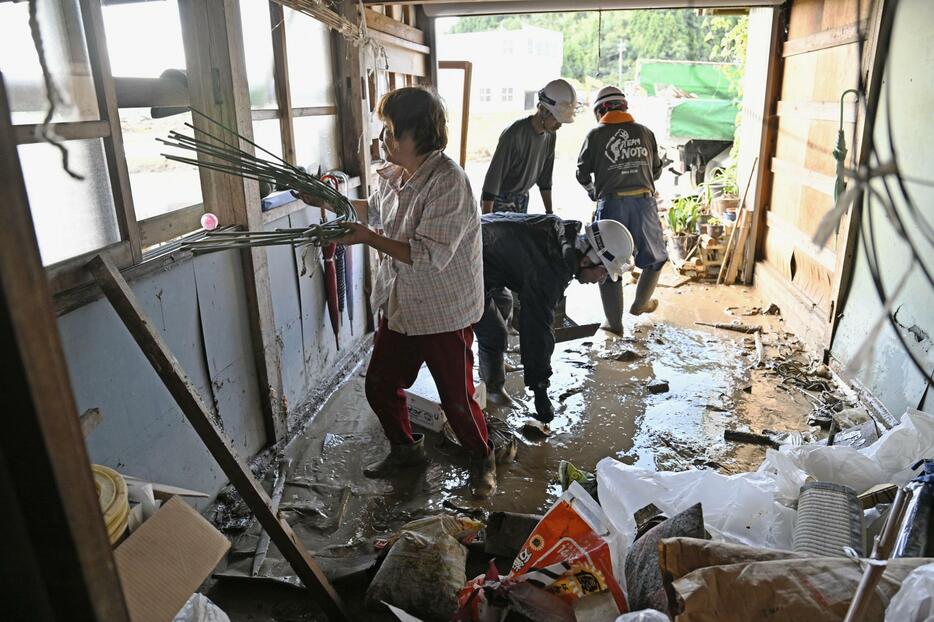 豪雨で浸水した自宅の車庫で、ボランティアらと後片付けする女性（左端）＝23日午前8時41分、石川県珠洲市