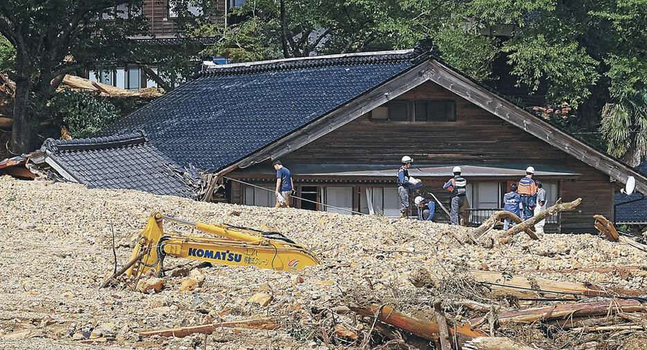 安否不明者の自宅を埋めた土砂の状況を確認する警察官と消防隊員＝２３日正午、珠洲市大谷町