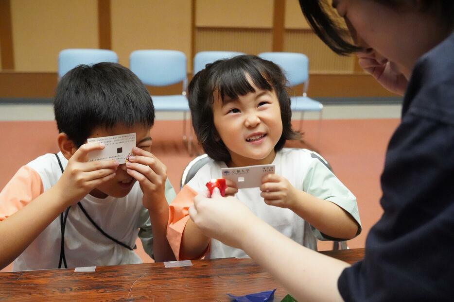 「虹が見えた」。名刺サイズのカードの小窓に取り付けられた回折格子フィルム越しに、点灯する発光ダイオードの光を観察する子ども＝兵庫県丹波篠山市網掛で