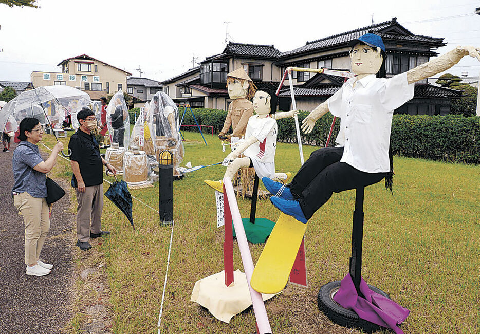 中山選手（右）、大堀選手（右から２番目）のかかしを眺める来場者＝高岡市中田中央公園