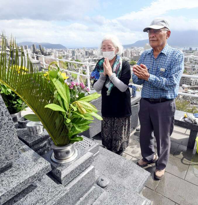 墓前で手を合わせる夫婦＝１９日、鹿児島市の郡元墓地