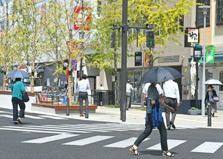 強い日差しに日傘を差して歩く人たちの姿が多く見られた＝11日午後、佐賀市