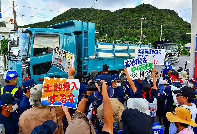 桟橋に次々とやって来る土砂を運ぶトラックを前に抗議する市民＝8月、名護市安和（喜瀨守昭撮影）