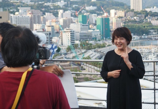 熱海市街地を背景にＰＲ動画の撮影をする小高さん＝熱海市和田浜南町