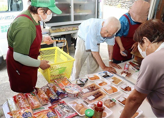 地区の空き倉庫に食材を並べ、高齢者の買い物をサポートするスタッフたち＝８月６日、朝日町笹川地区