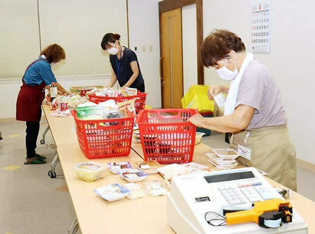 手際よく総菜や菓子などをテーブルに並べるスタッフ＝８月６日、ケアハウス「みんなの家」