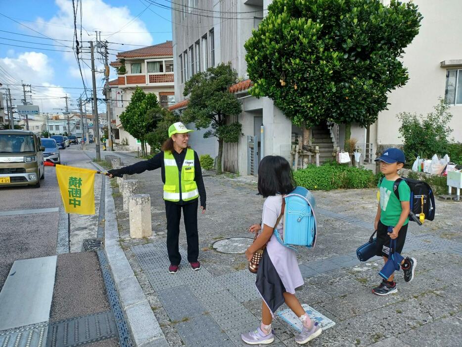 黄色の旗を手に登校の安全見守りをする中山順子さん＝８月30日、那覇市首里真和志町の城西小学校前