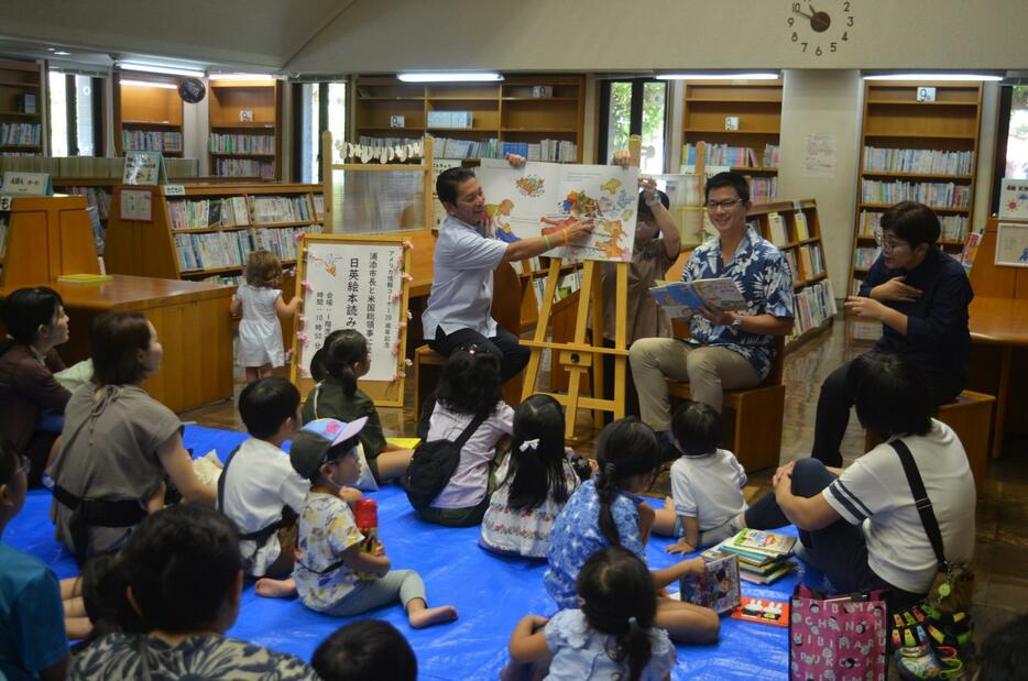 子どもたちに日本語と英語で絵本を読み聞かせる松本哲治市長とアンドリュー・オウ在沖米国総領事＝7日、浦添市立図書館