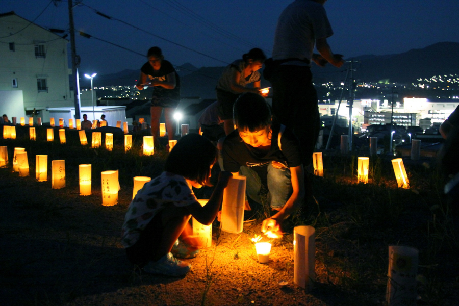 41人の犠牲者が出た八木3丁目地区で、熊本や東日本大災害の被災者からも寄せられたメッセージが書かれた灯籠に火を灯す山城久美さん（35）と、ほたるさん（5）2016年8月20日