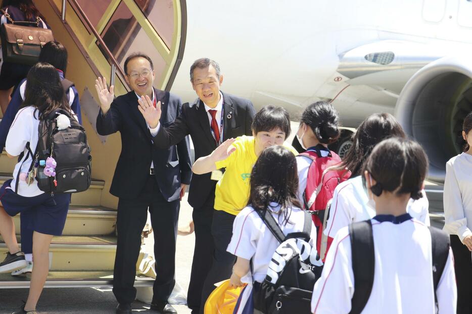 周遊フライトへ向かう児童たちを見送る日航成田空港支店の真行寺誠副支店長（左）ら＝24日午前、千葉県成田市