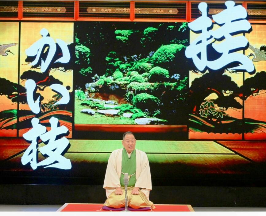 大型スクリーンに映し出された「桂かい枝」を背にした舞台上の本人