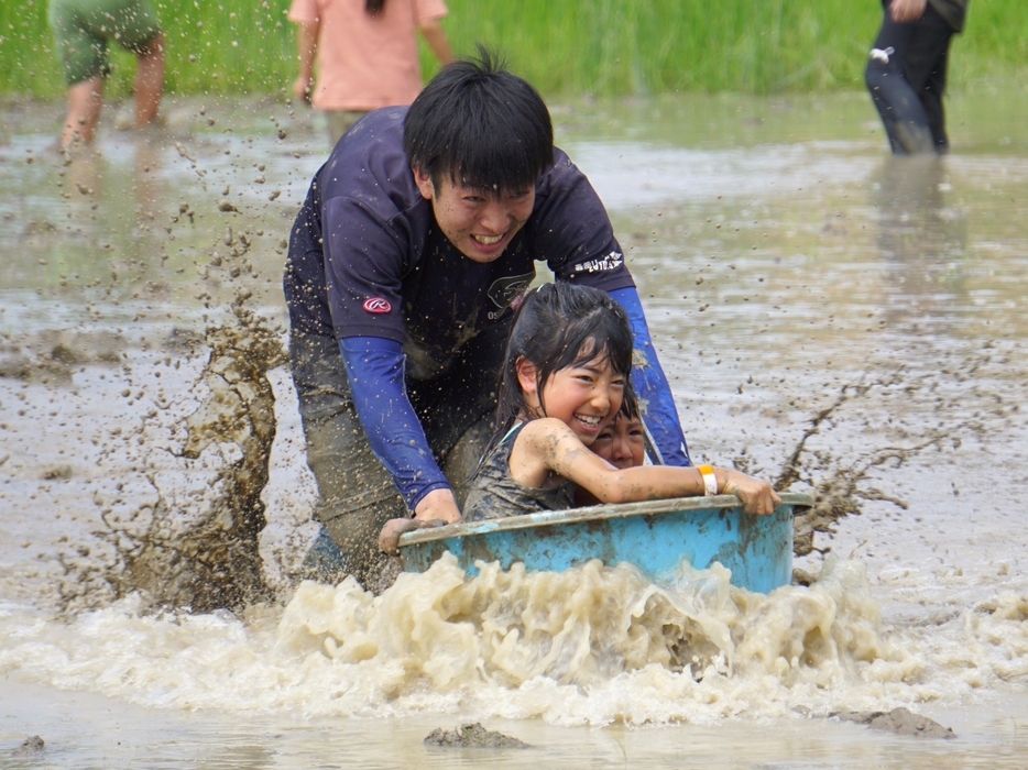 泥田の中でたらいを押してもらって楽しく遊ぶ子どもたち＝兵庫県丹波篠山市小田中で