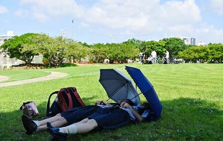 テスト期間の学生たちは、リフレッシュで公園へ。女子生徒は日傘を差してお昼寝中＝１５日、那覇市・新都心公園（喜屋武綾菜撮影）