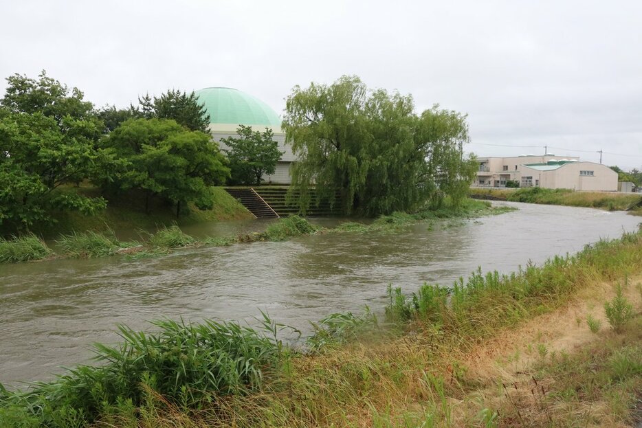大雨の影響で増水した吉田川。吉田科学館の裏の階段が途中で水没している＝２３日午後４時半ごろ、黒部市吉田