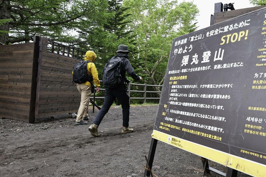 富士山の山開きを前に、山梨県側から登山に向かう人たち。手前は「弾丸登山」への注意を呼びかける看板＝30日午前